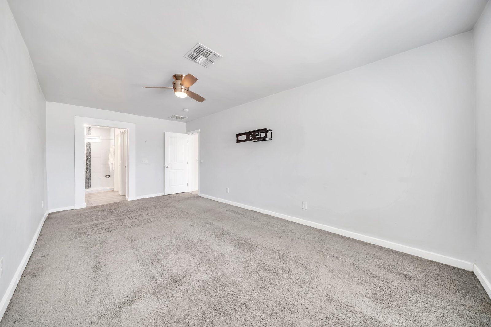 Carpeted primary bedroom with a ceiling fan and a doorway through to its own bathroom